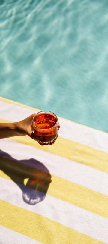 A hand holding a cocktail at a pool