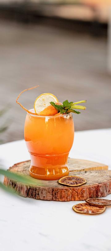A bright orange citrus cocktail with a green garnish, served on a wood slab
