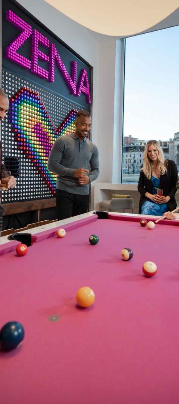 A group of people playing pool on a bright pink pooltable
