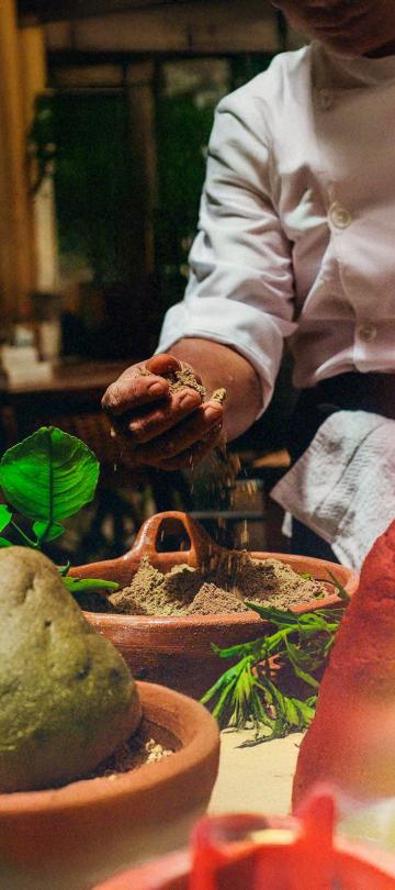man wearing a white shirt puts hand in bowl of brown cooking spices