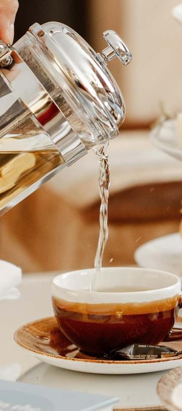 A person pours tea next to a tea tower with sandwiches and macarons