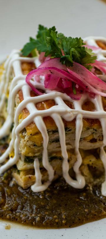 A tarte topped with pickled onions and cilantro, drizzled with crema and served on a sauce base