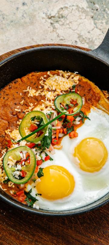 eggs and red sauce with toppings in cast iron pan 