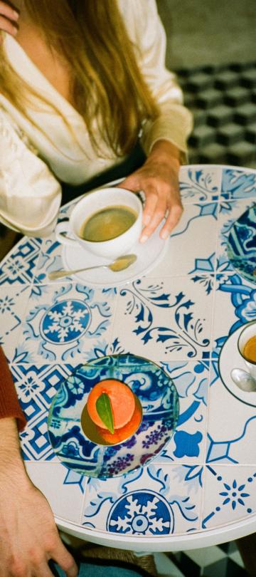 two people sit at blue printed tabletop with coffee and desserts