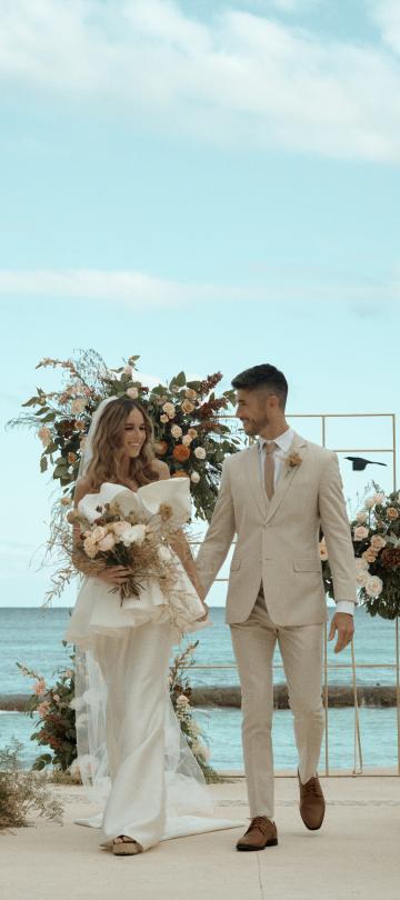 A newly married couple walk hand in hand back down the aisle, smiling at one another. 