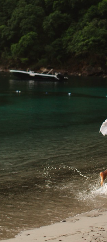 Two women run down a beach, surrounded by the rainforest.
