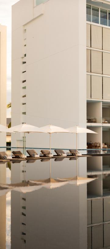 A mirror-like pool with the hotel and lounge chairs in the background.