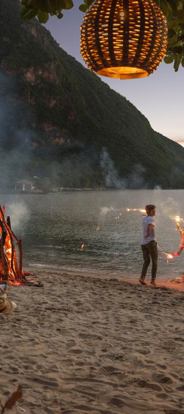 A family dances on the beach with sparklers at dusk. 