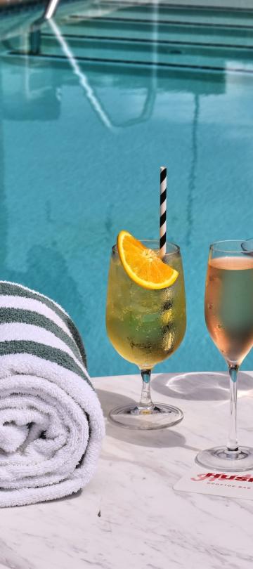 Three cocktails on a poolside table next to a rolled up towel, at Hush, the rooftop patio bar at Viceroy Washington DC