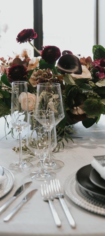A beautifully decorated table with plates, glasses, and a elegantly decorated bouquet showpiece in the center. 