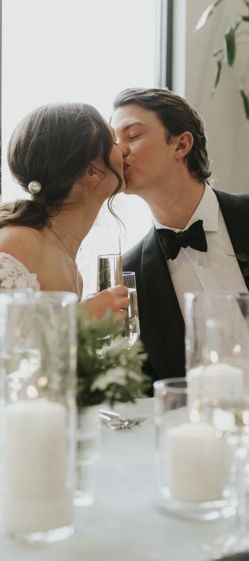 A bride and groom celebrating their wedding with a kiss while the guests toast