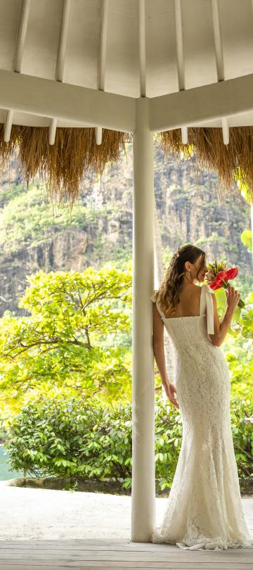 Une femme debout, un bouquet à la main, vêtue de sa robe de mariée