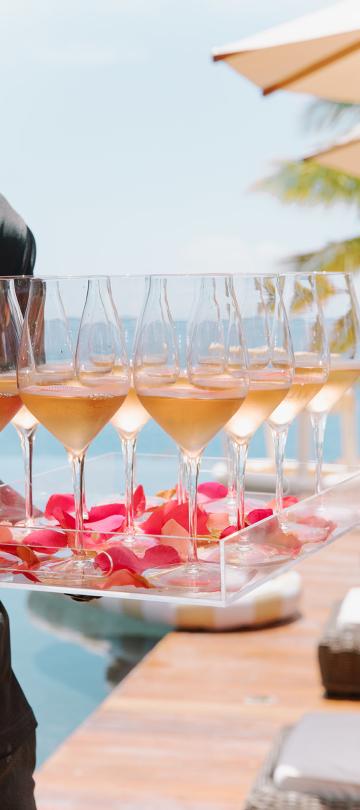 Des verres à vin disposés sur un plateau parsemé de pétales de fleurs