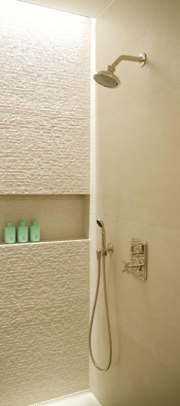 Luxurious walk-in hotel shower featuring textured beige tile, modern chrome fixtures, and bath products in a niche.