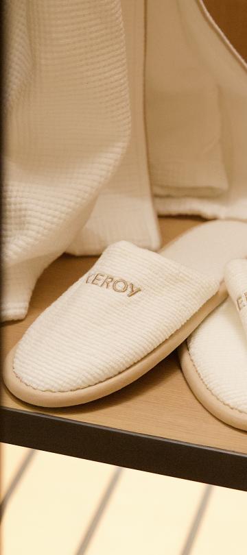 Close-up of white plush slippers embroidered with text inside an open wooden wardrobe shelf.