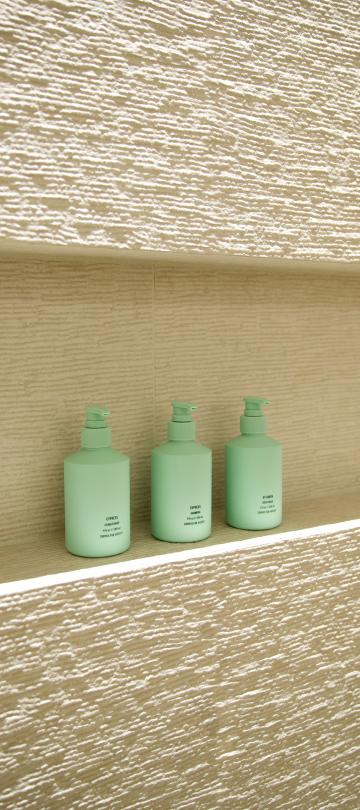Three mint green amenity bottles sitting inside an illuminated tiled shower wall niche.