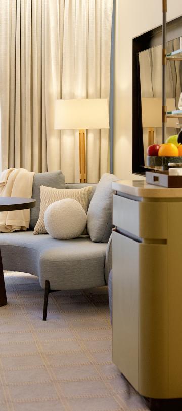 Elegant hotel room suite featuring a curved sofa, small dining table with champagne, and a king bed.