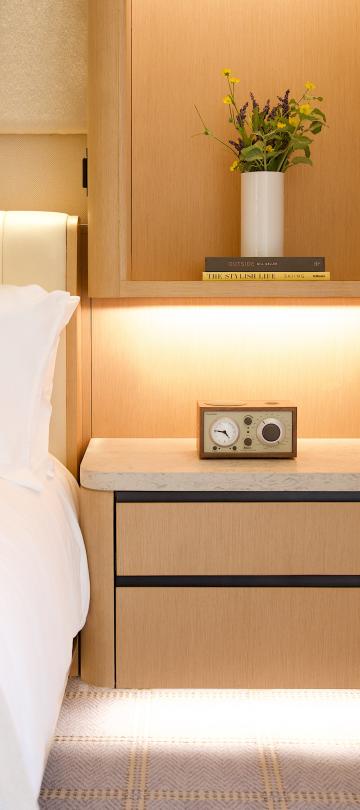 Close-up of a hotel bedside table with a vintage radio, warm under-cabinet lighting, and fresh flowers.