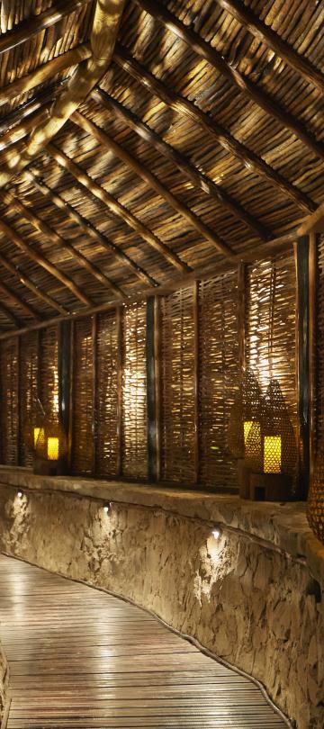 A long hallway in a thatched roof building illuminated by candles