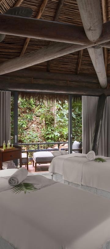 An open air massage room with two tables and a rainforest landscape
