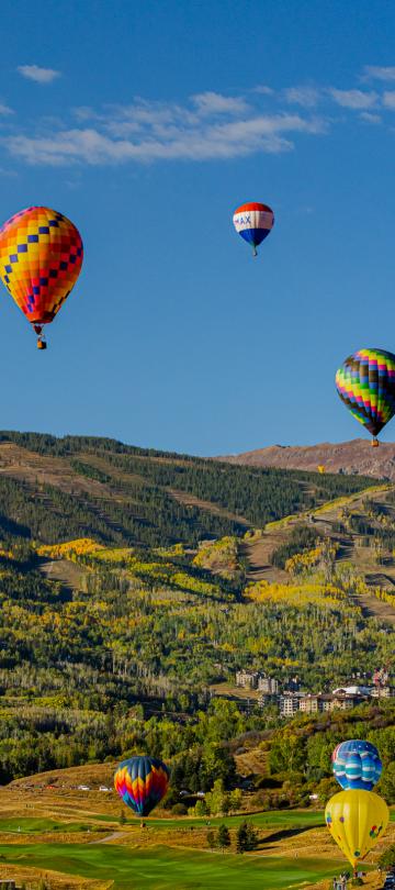 Une douzaine de montgolfières survolent la ville de Snowmass, avec les montagnes verdoyantes en arrière-plan