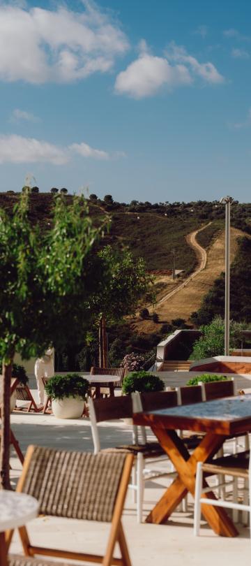 Um terraço ao ar livre com mesas de jantar e a paisagem rural do Algarve como pano de fundo