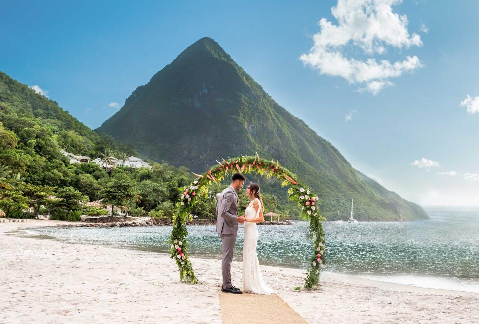 bride and groom stand under floral arch on beach