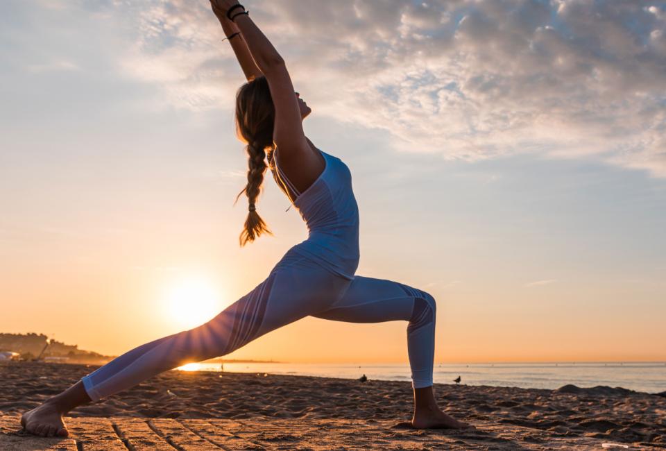 A woman does yoga on Santa Monica beach at sunset