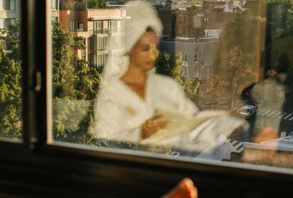 The reflection of a woman in a spa robe reading in a window