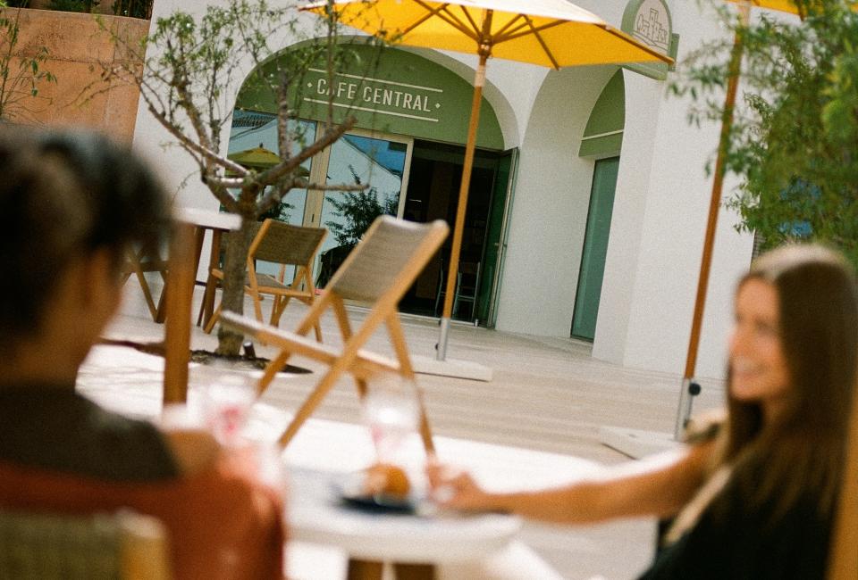 two people sit at tables in courtyard under yellow umbrella