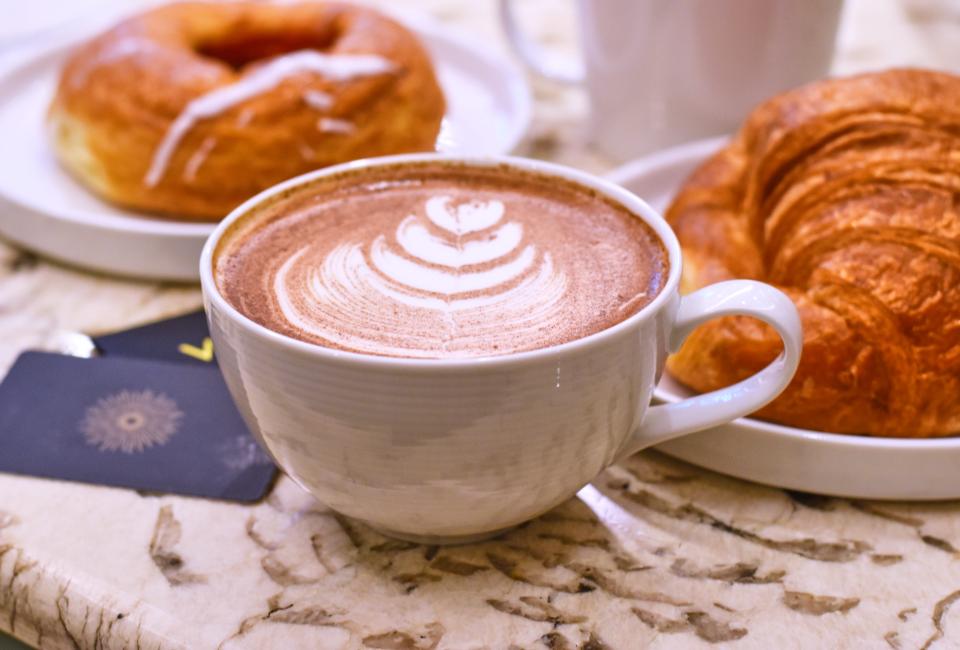 A latte with flora latte art on a table next to plates of croissants and other pastries