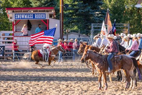 people carrying flags ride horses at rodeo 