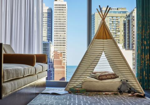 A triangular teepee-style children's pop-tent set up in a hotel room looking out on the Chicago skyline