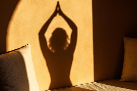 The shadow of a person doing a yoga pose on a stone wall