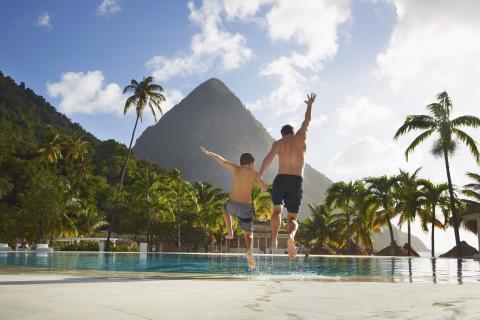 A father and son jumping into the pool at Viceroy Sugar Beach with beautiful mountains ion the foreground