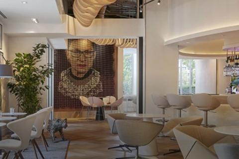 A seating area within Hotel Zena featuring chairs, tables, and a large piece of artwork on the far wall.