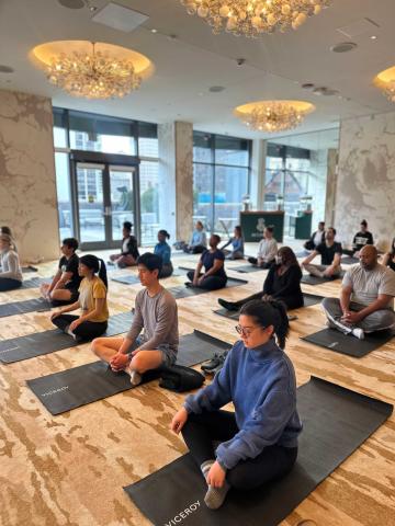 group class of people sitting cross-legged on black yoga mats