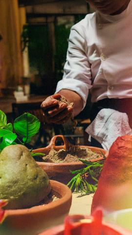 man wearing a white shirt puts hand in bowl of brown cooking spices