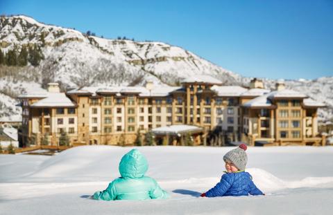 Two toddlers in snowsuits sit in the snow outside Viceroy Snowmass