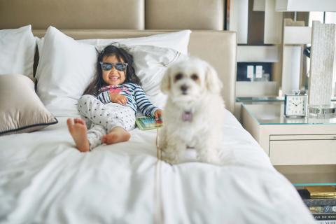 A girl in sunglasses and a small white dog relaxing on a bed at Sugar Beach