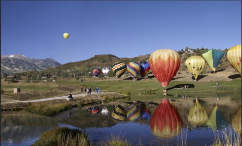 Hot air baloons float in the air, while others prepare to lift off.