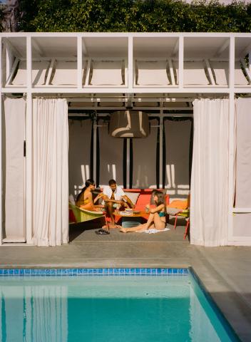 Three friends sit in a cabana, sipping drinks and talking.