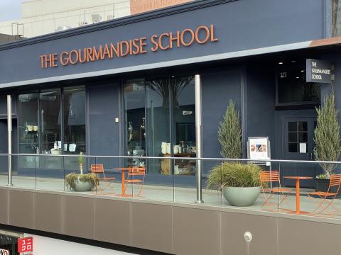 The exterior of the Gourmandise School, a single-story chic grey building with the school's name in modern golden lettering.