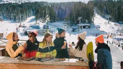 A group of skiers relaxing on a patio overlooking the mountain