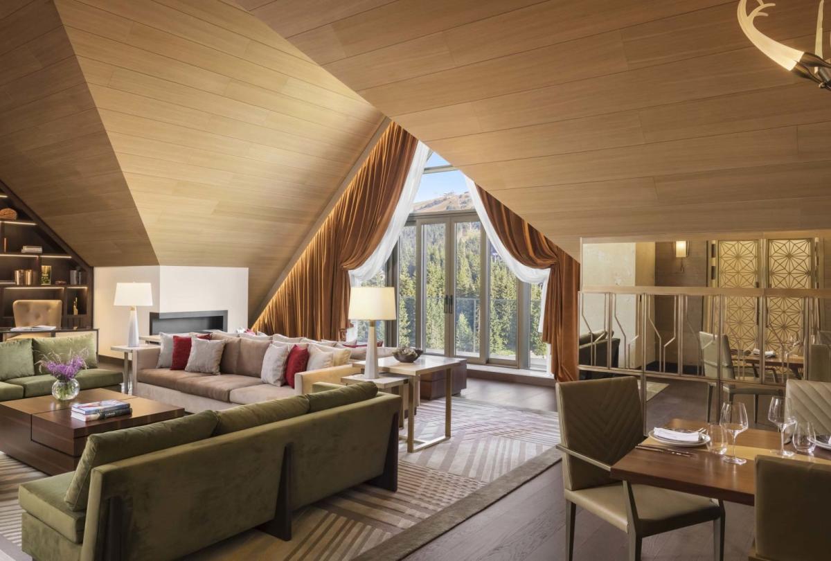 The living space of a penthouse suiter with 2 couches, a large dining table, a floor to ceiling bookshelf and unique drop ceilings A washroom with a large double sink vanity and a soaker tub in a penthouse suite at Viceroy Kopaonik Serbia