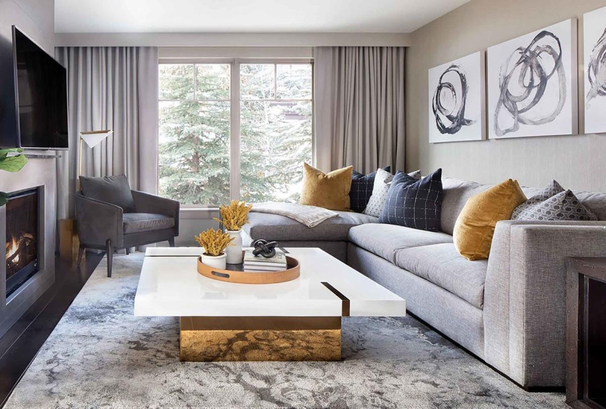 The large living area with a white marble coffee table, l-shaped couch and a large television in a Pinnacle Two Bedroom Premium Residence at Viceroy Snowmass