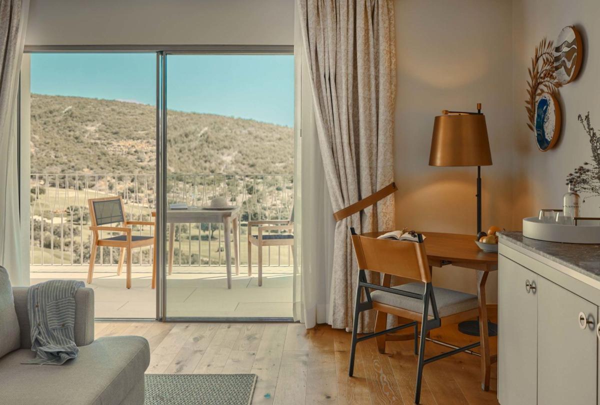 The living space with a couch, dresser , chair, and a balcony in a valley view room at Viceroy Ombria Algarve