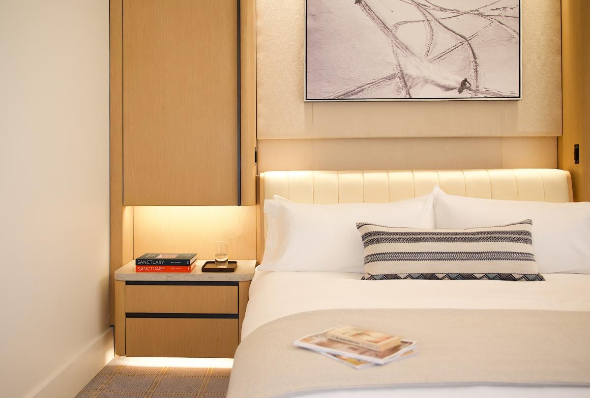 Hotel bed with white linens and a striped throw pillow next to a nightstand with books and water.