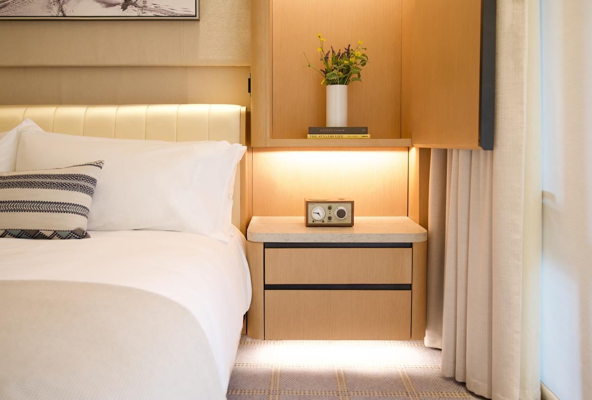 Close-up of a hotel bedside table with a vintage radio, warm under-cabinet lighting, and fresh flowers.