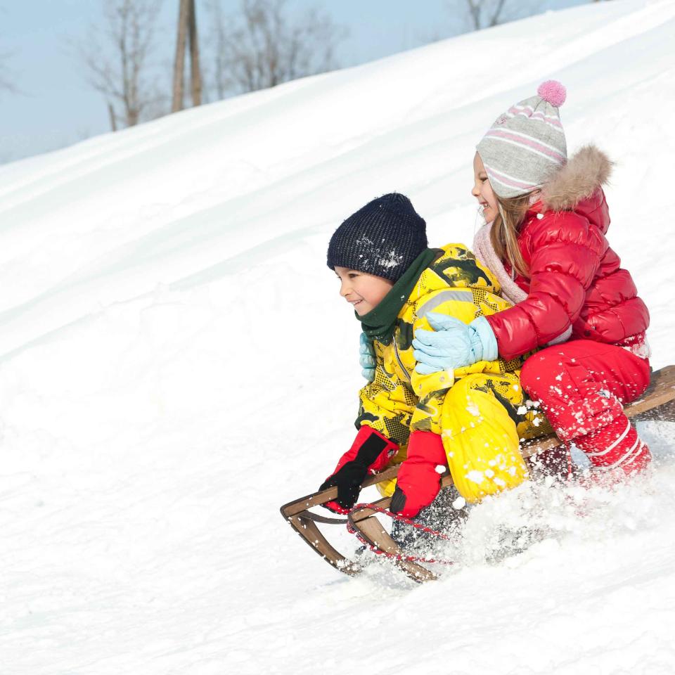 Two small children descend a small hill in a wooden sled